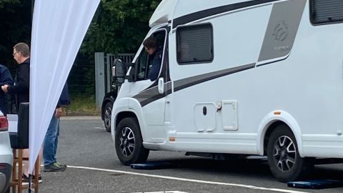 Ein weißes Wohnmobil fährt gerade von den Messplatten der Radlastwaage des TÜV Rheinland herunter. Links neben dem Wohnmobil steht ein Mitarbeiter des TÜV.
