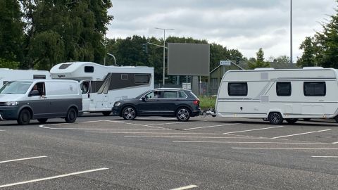 Auf einem Parkplatz hat sich eine Schlange aus wartenden Wohnmobilen und Wohnwagen gebildet. 