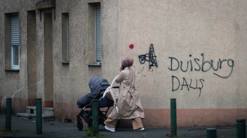 Frau mit Kinderwagen geht an einem Haus vorbei. Auf der Hauswand befindet sich ein Graffiti Schriftzug "Duisburg Dalis"